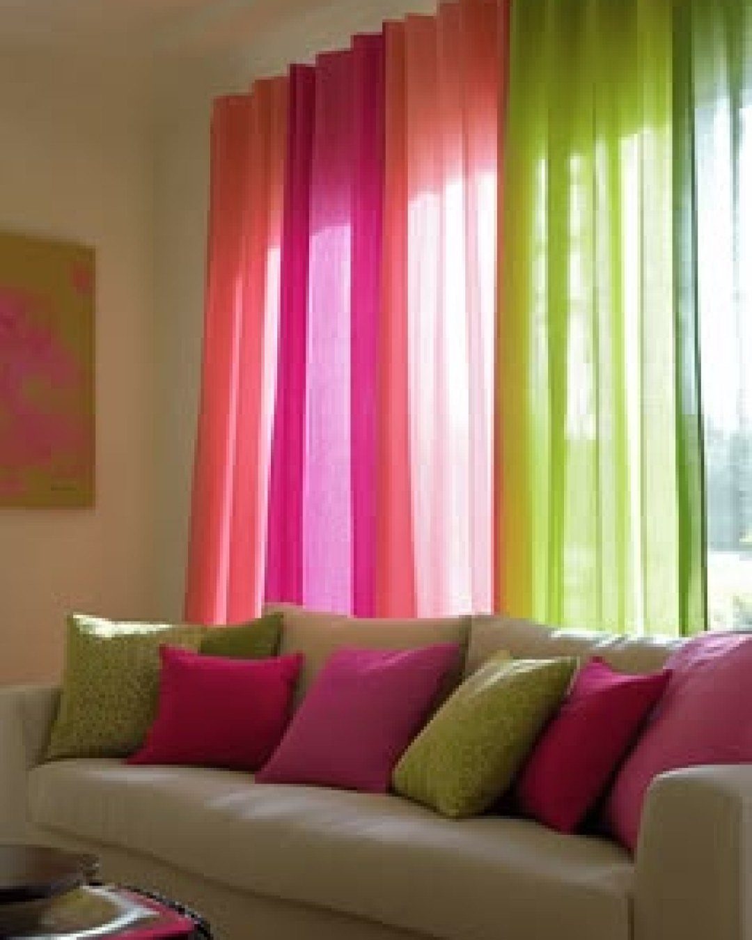 Colorful sheer curtain panels in pink and lime green hanging behind a white sofa with matching pillows.