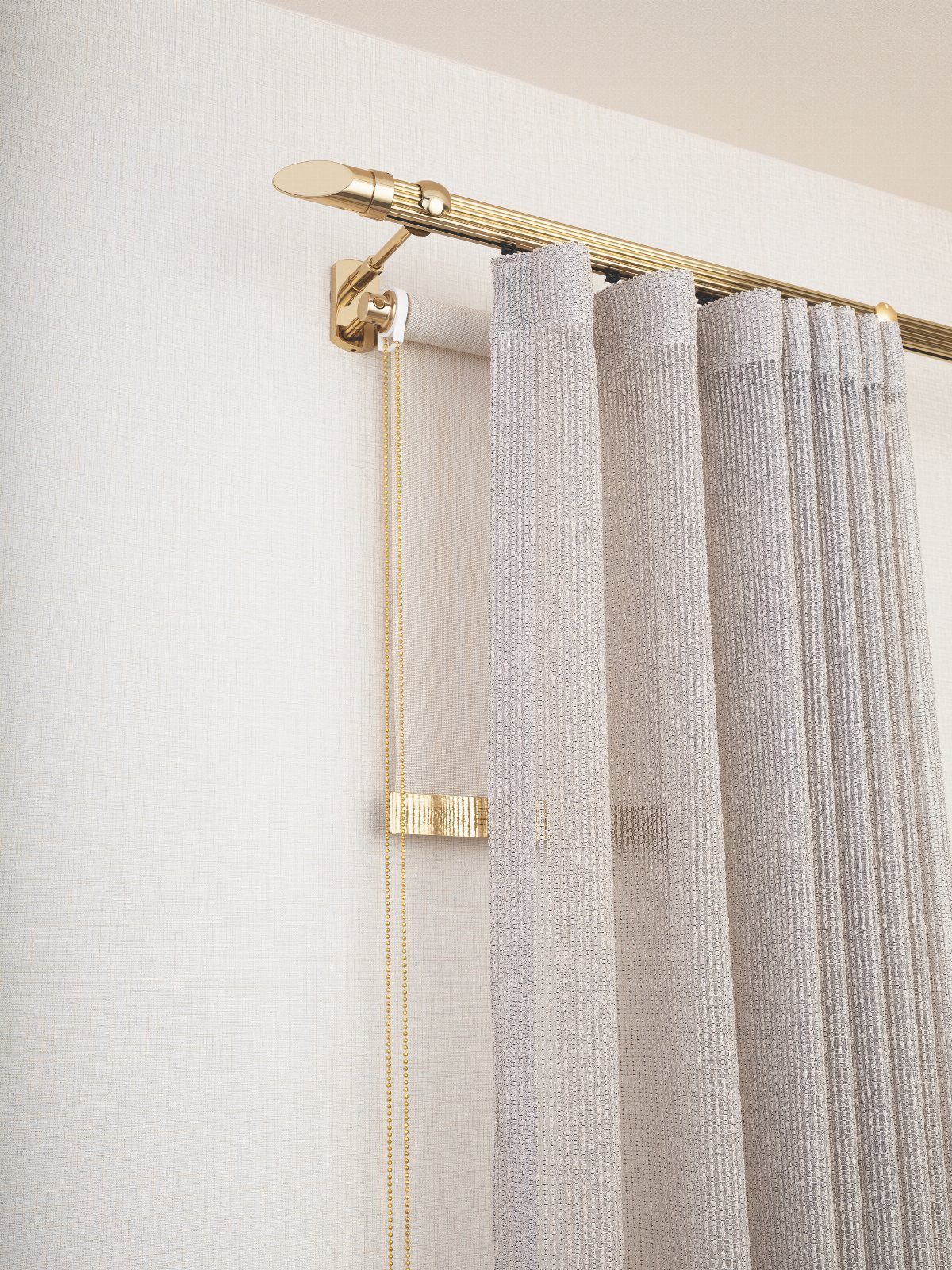 Gold decorative curtain rod holding pleated grey curtains against a white textured wall.