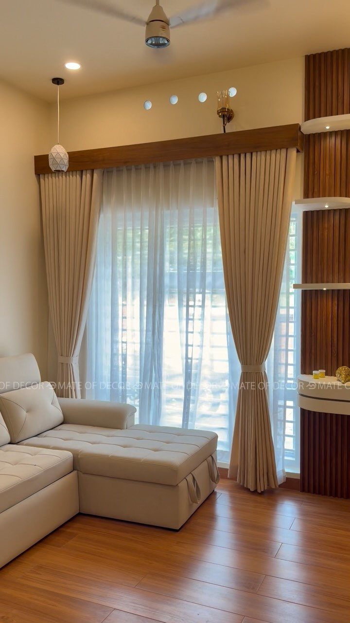 Beige heavy drapes tied back over white sheer curtains covering a large window in a living room.