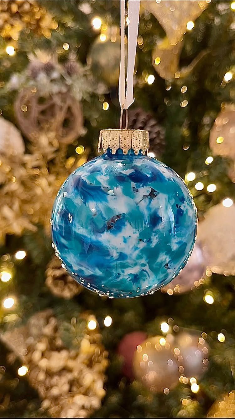 7 Ideas for Decorating Clear Ornaments with Glitter, Crayon & More 2 A blue and white marbled clear glass ornament hanging on a lit Christmas tree.