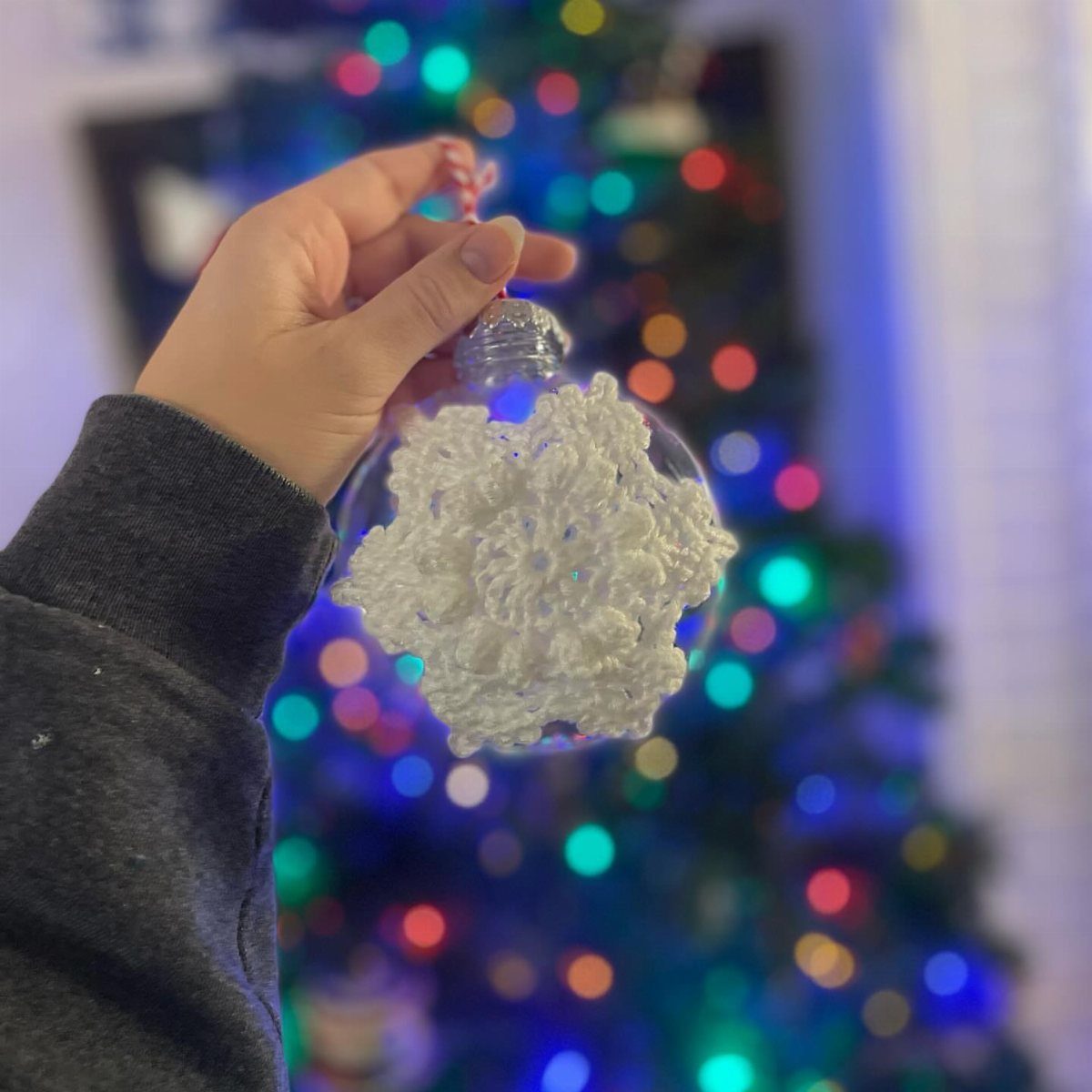 7 Ideas for Decorating Clear Ornaments with Glitter, Crayon & More 6 A hand holding a clear ornament with a white snowflake inside against a blurred Christmas tree.