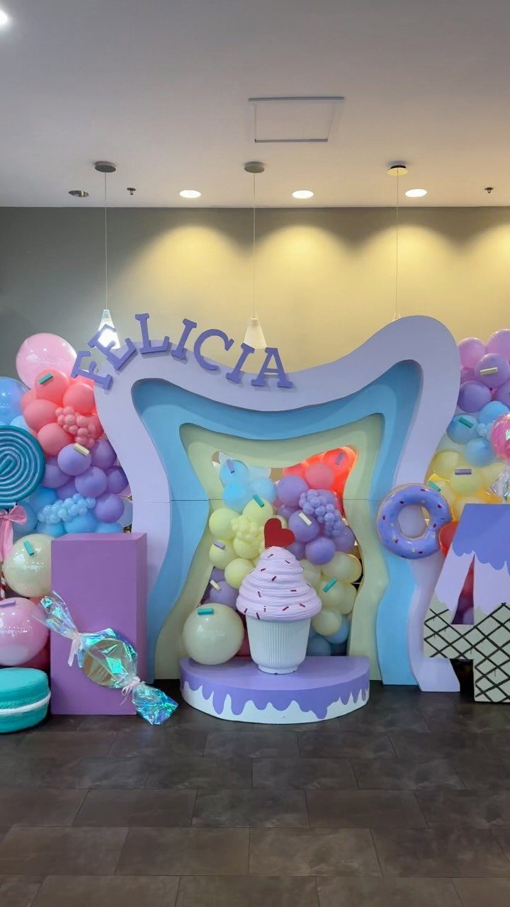 DIY Candyland Decorations: 10 Creative Party Ideas 4 Pastel balloon garlands and oversized candy props decorate a large purple backdrop for a birthday party.