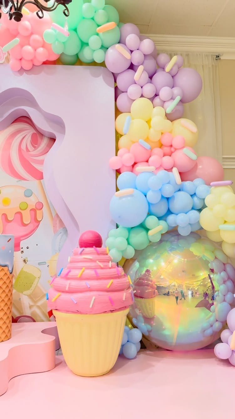 DIY Candyland Decorations: 10 Creative Party Ideas 8 A large pink cupcake prop stands in front of a pastel balloon garland and backdrop.