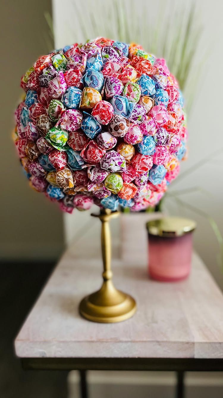 DIY Candyland Decorations: 10 Creative Party Ideas 6 A colorful sphere of wrapped candies mounted on a gold pedestal stand on a wooden table.