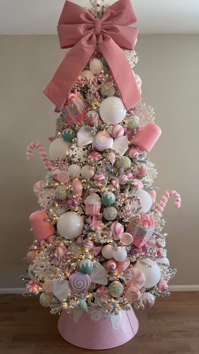 A Christmas tree decorated with pink, white, and mint green candy-themed ornaments and large bows.
