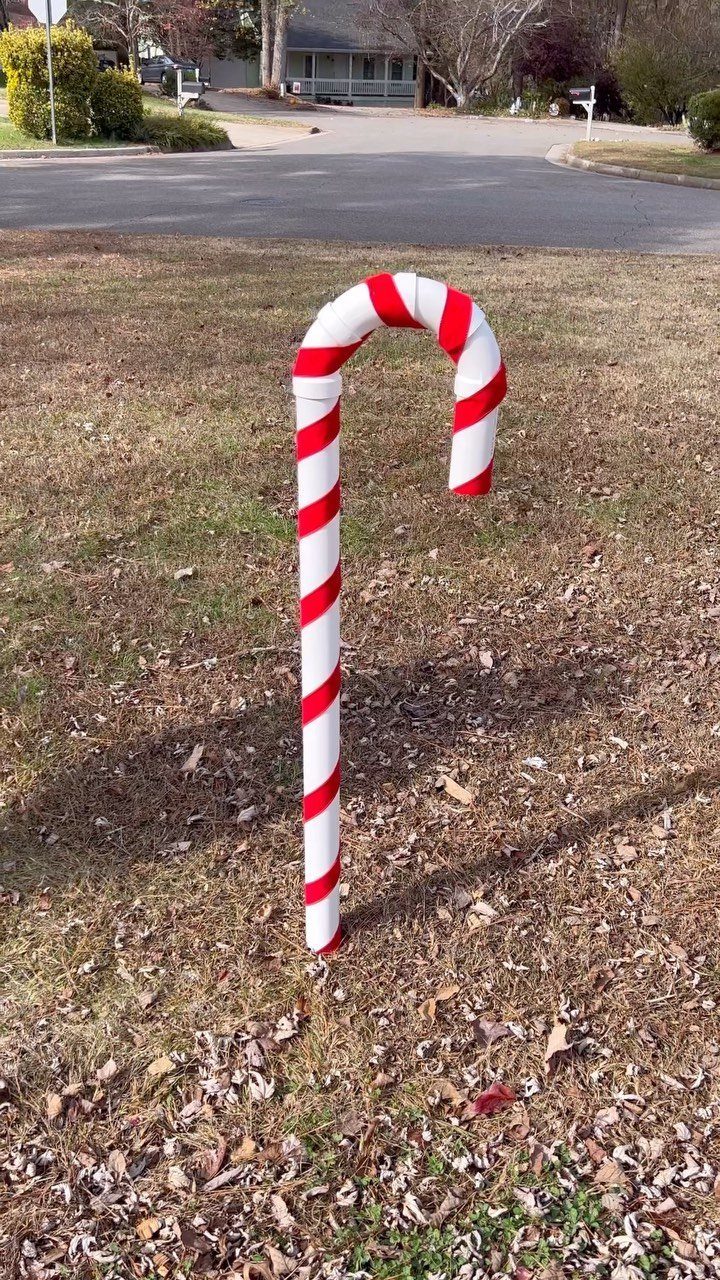 A large red and white striped candy cane decoration standing in a grassy yard.