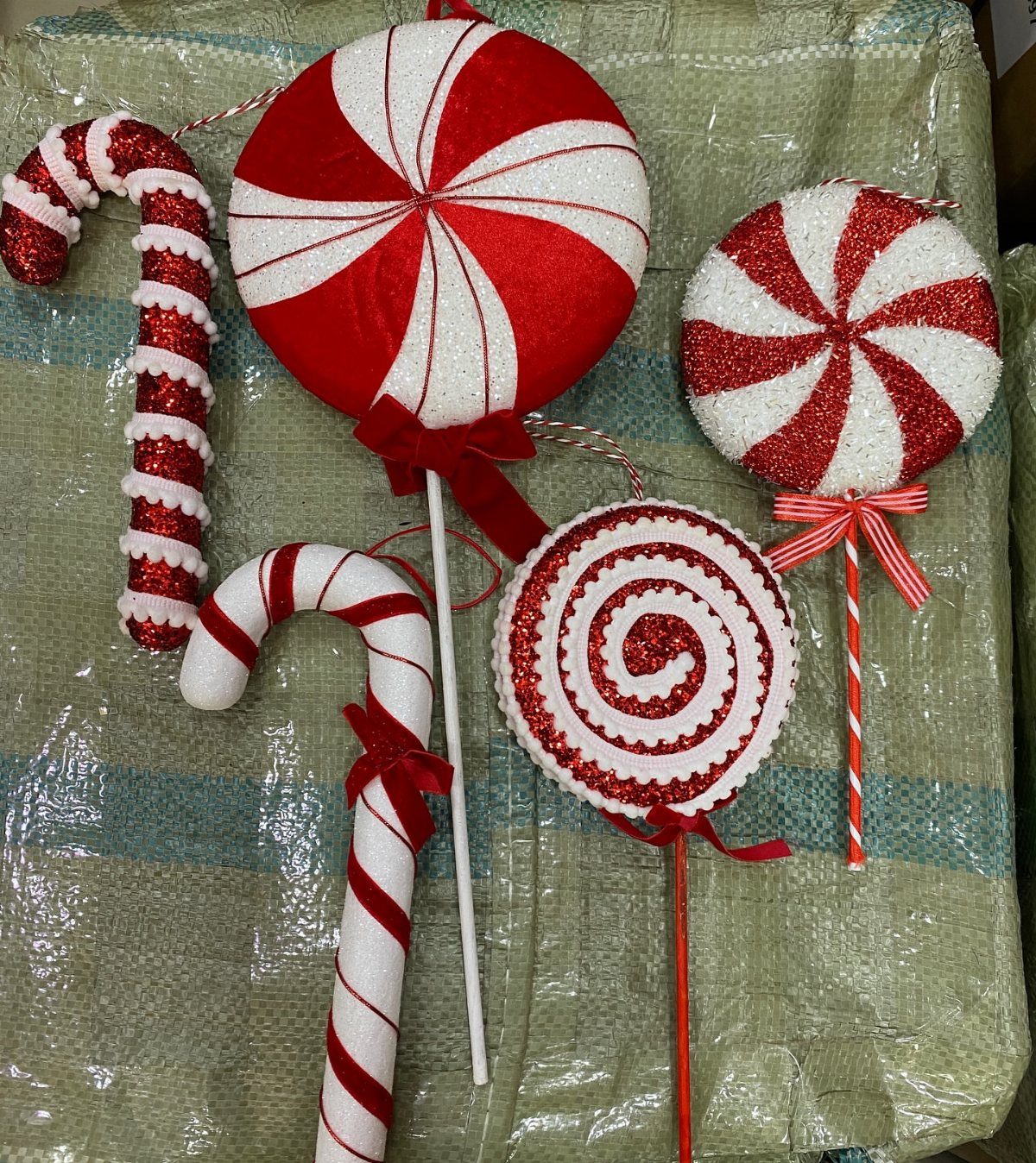 Red and white glittery decorative lollipops and candy canes on sticks lying on a green background.