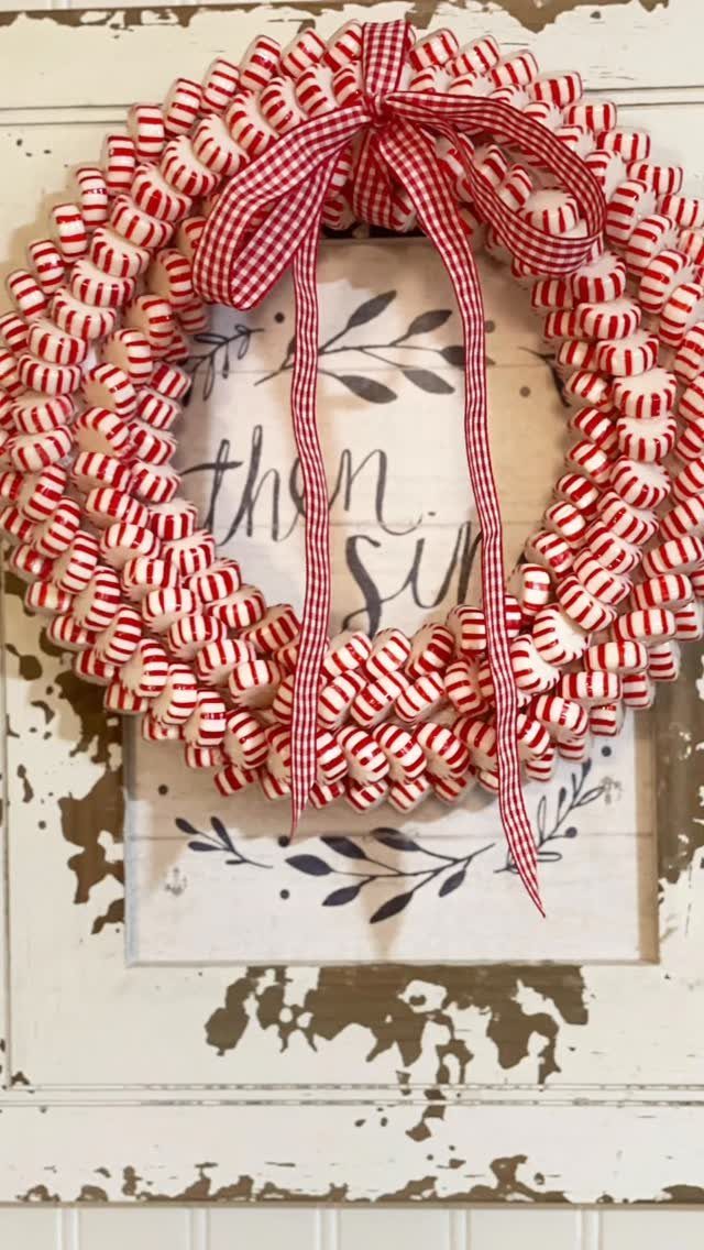 A peppermint candy wreath with a red and white checkered bow on a white wooden background.