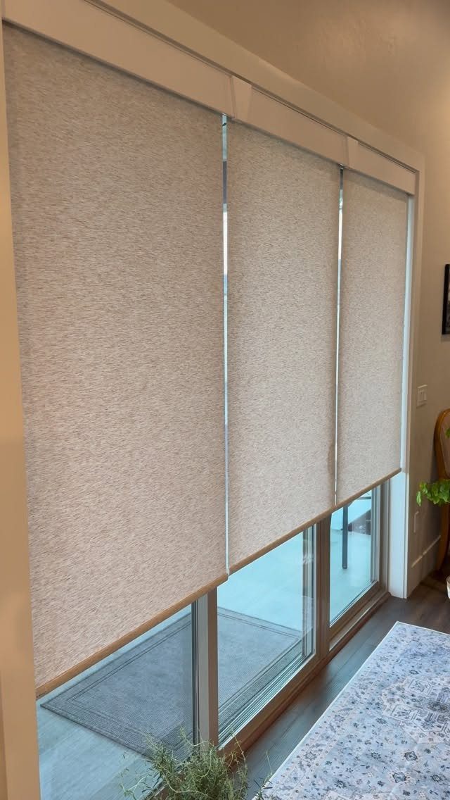 10 DIY Window Covering Ideas for a Quick Upgrade 2 Three beige textured roller shades covering a large sliding glass door in a bright room.