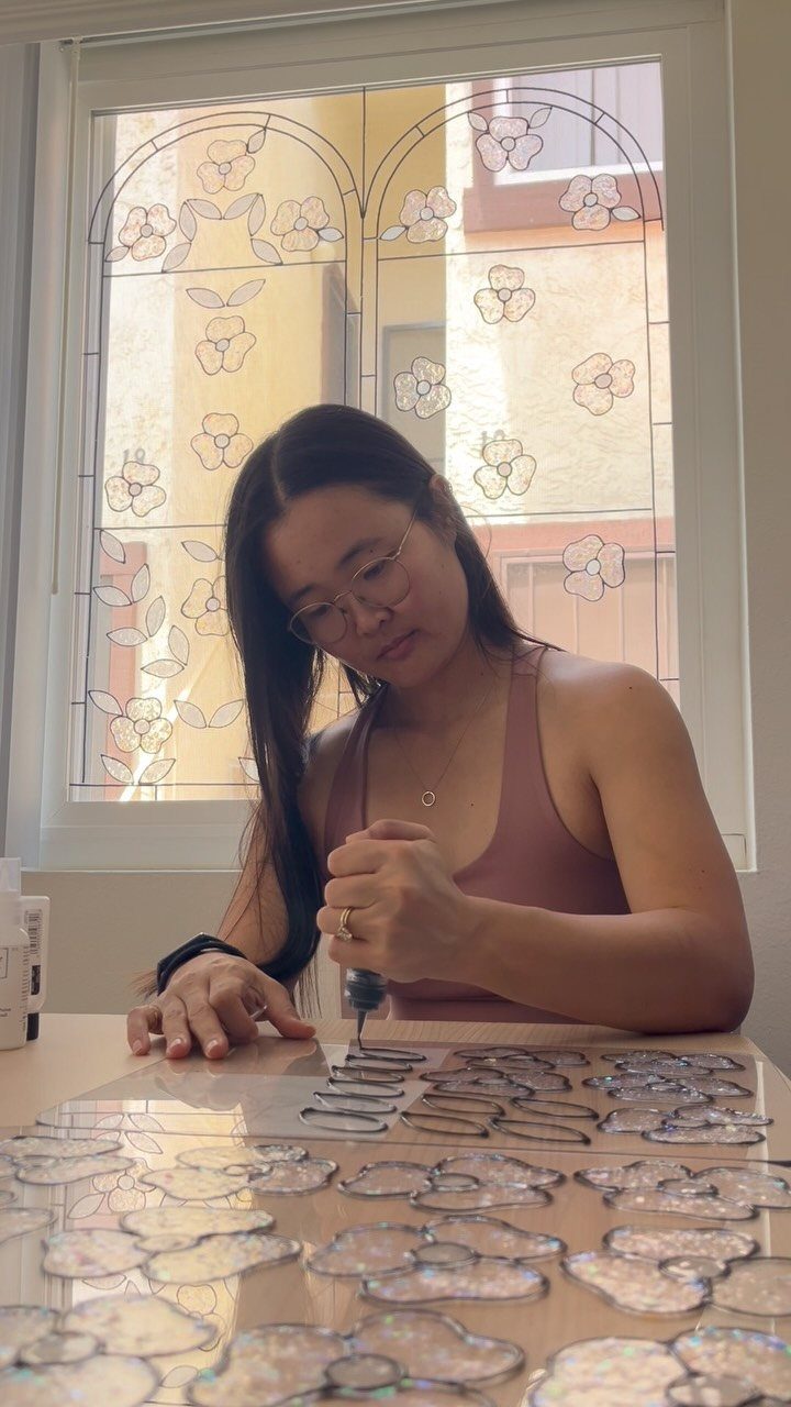 10 DIY Window Covering Ideas for a Quick Upgrade 7 A woman working on a DIY stained glass floral design panel at a table.