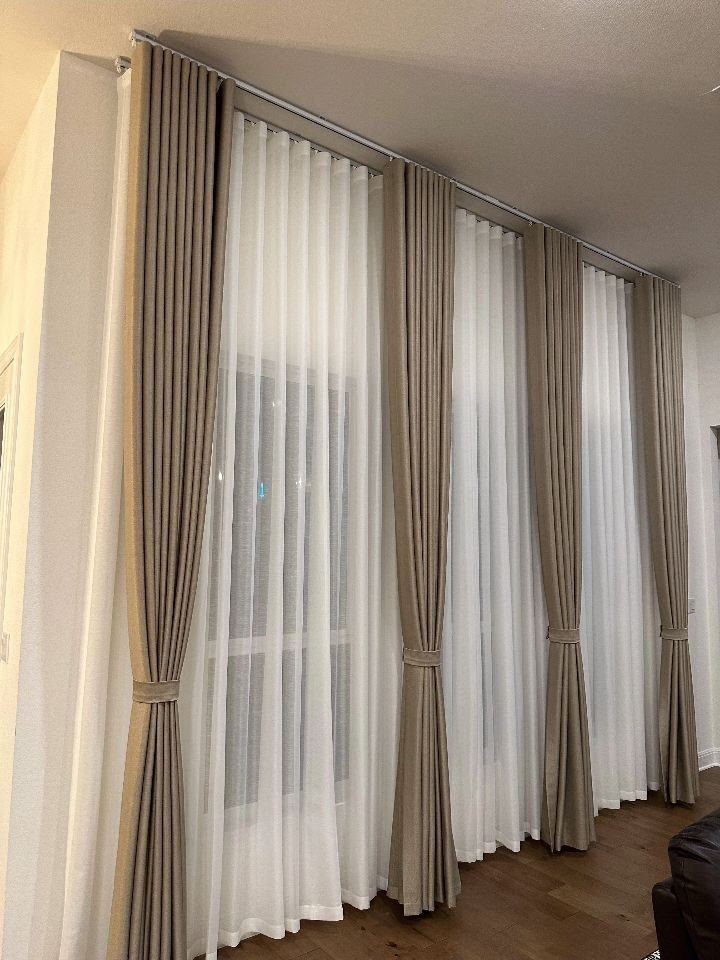 10 DIY Window Covering Ideas for a Quick Upgrade 9 Taupe drapes tied back in front of long, sheer white curtains covering a large window.