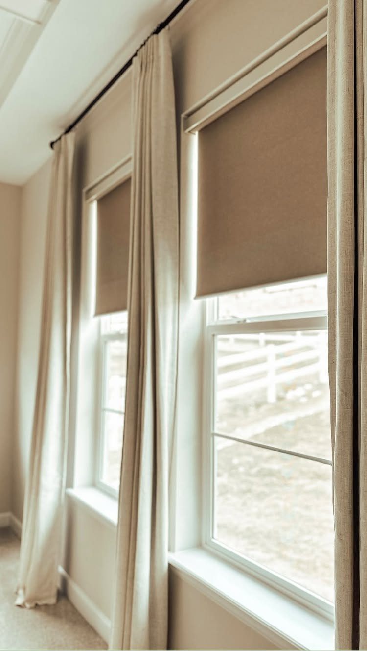 10 DIY Window Covering Ideas for a Quick Upgrade 5 Beige roller shades paired with long cream curtains hanging on a black rod by windows.