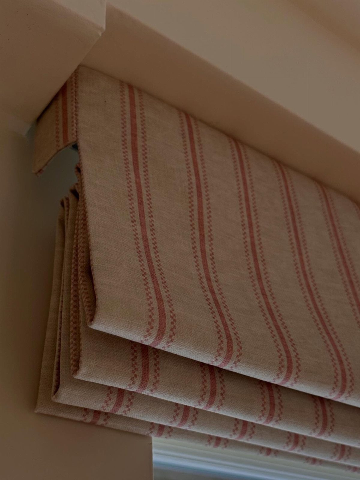 10 DIY Window Covering Ideas for a Quick Upgrade 1 A beige Roman shade with red vertical stripes hanging over a white window frame.