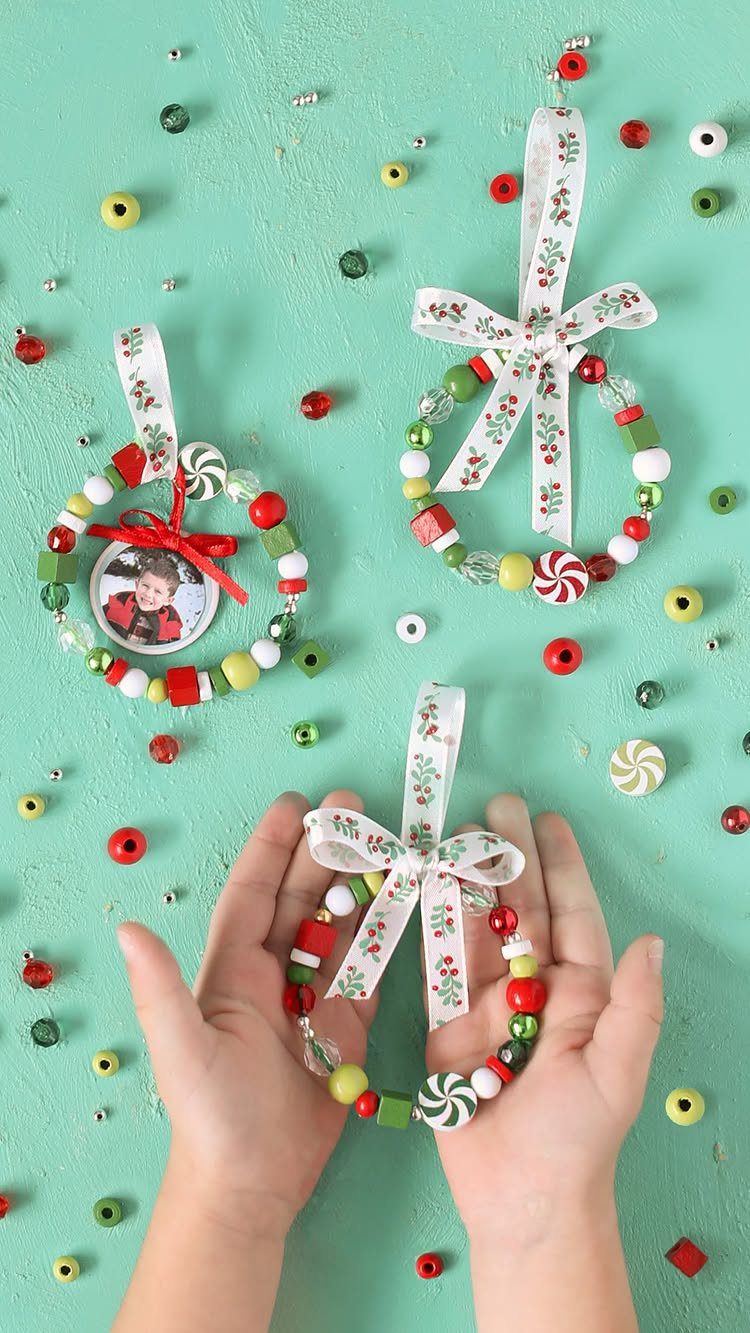 Three colorful beaded wreath ornaments with patterned ribbons resting on a mint green background.