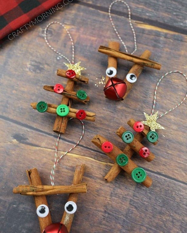 Cinnamon stick Christmas ornaments decorated with colorful buttons, bells, and stars on a wooden background.