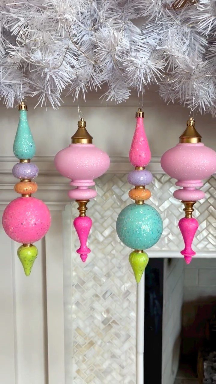 Four colorful glittery Christmas ornaments hanging from the branches of a white artificial tree.
