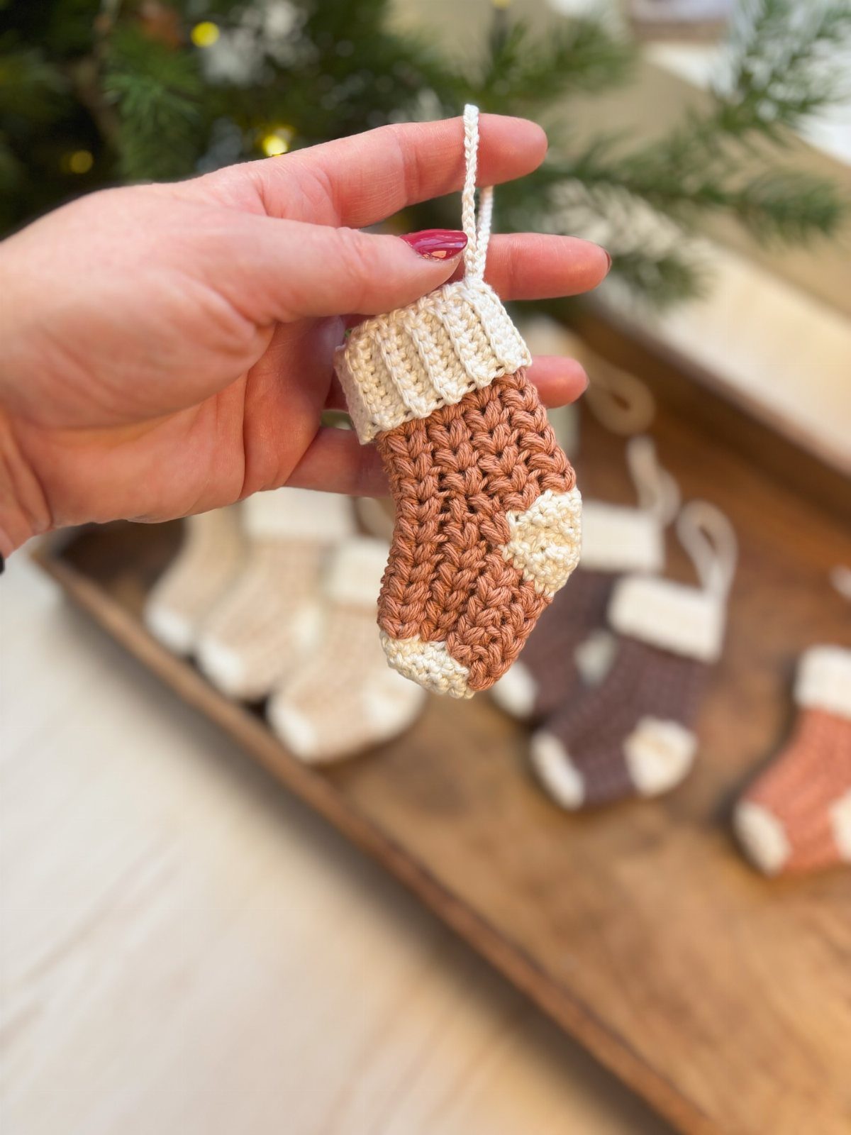 A hand holding a small crocheted cream and terracotta Christmas stocking ornament.