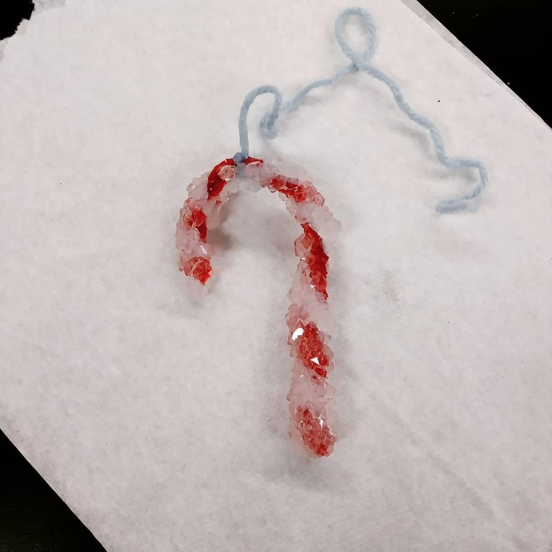 A red and white crystal-covered candy cane ornament on a white paper towel.