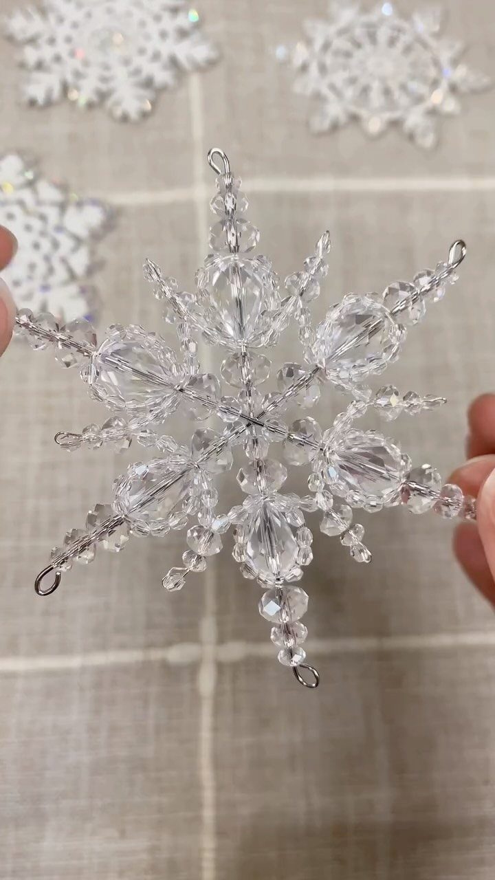 A person holding a sparkling crystal snowflake ornament against a neutral background.