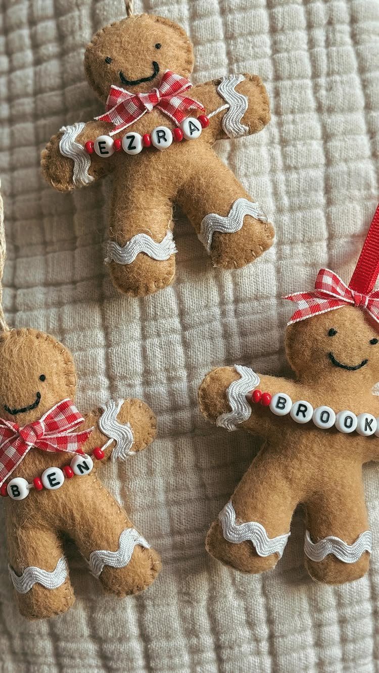 Three felt gingerbread man ornaments with red bows and personalized letter beads hanging on fabric.