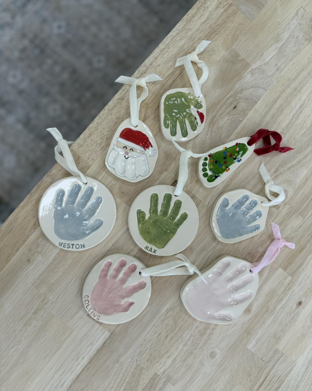 Ceramic ornaments with colorful handprints and names resting on a light wooden table.