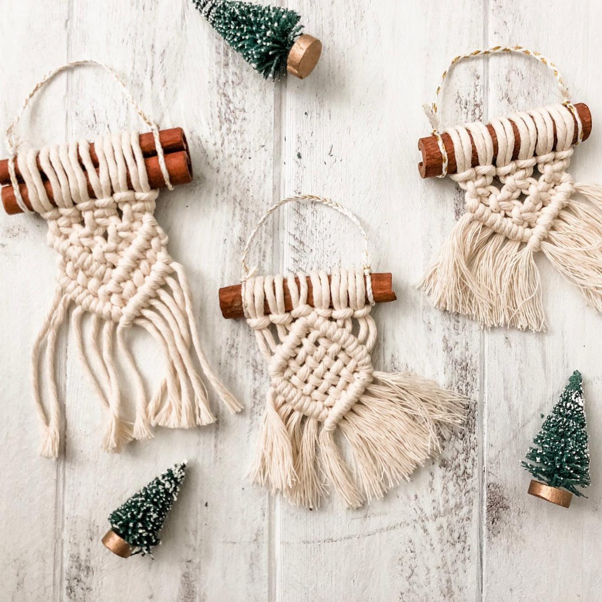 Three macrame ornaments made from cinnamon sticks on a white wooden background.