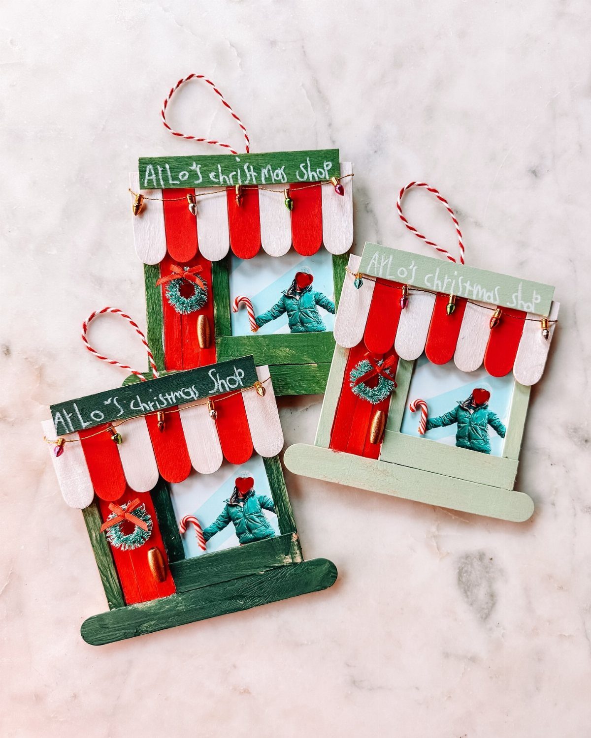 Three handmade popsicle stick shop ornaments with red and white striped awnings on a marble surface.