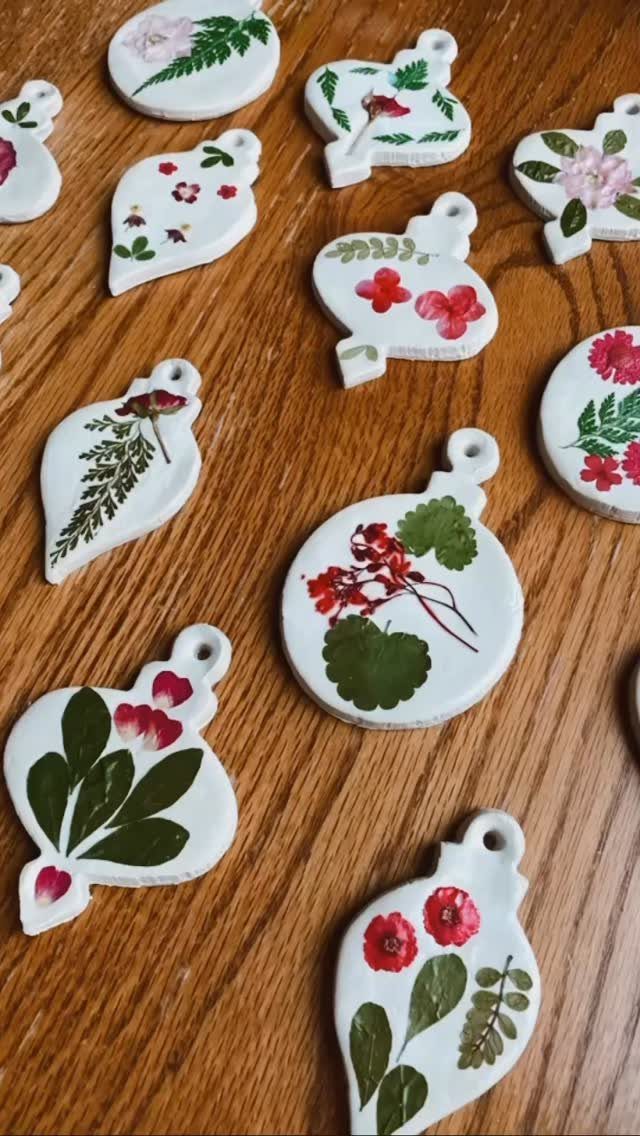 White ceramic ornaments decorated with colorful pressed flowers and green leaves on a wooden table.