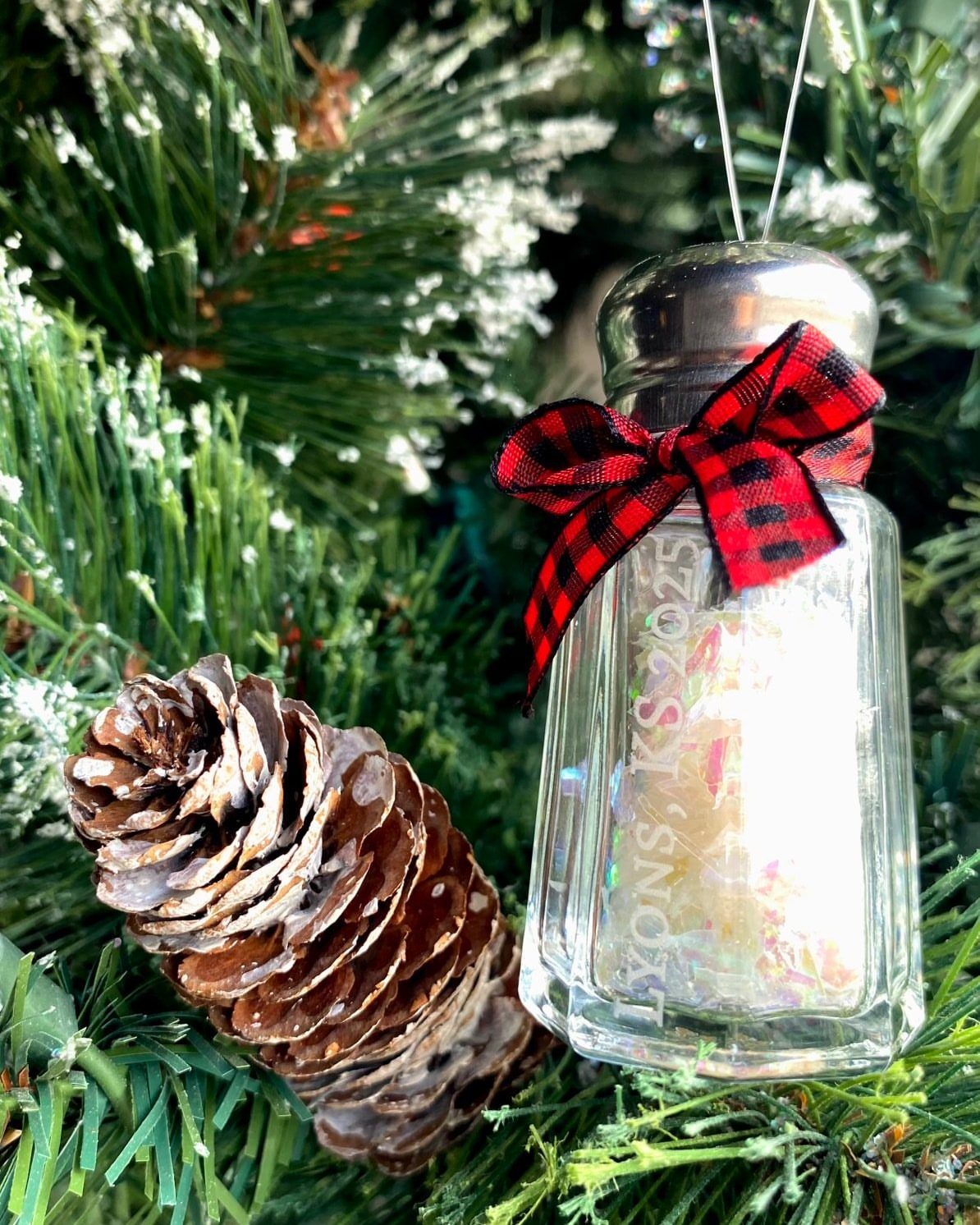 A glass salt shaker ornament with a red plaid bow hanging on a Christmas tree.