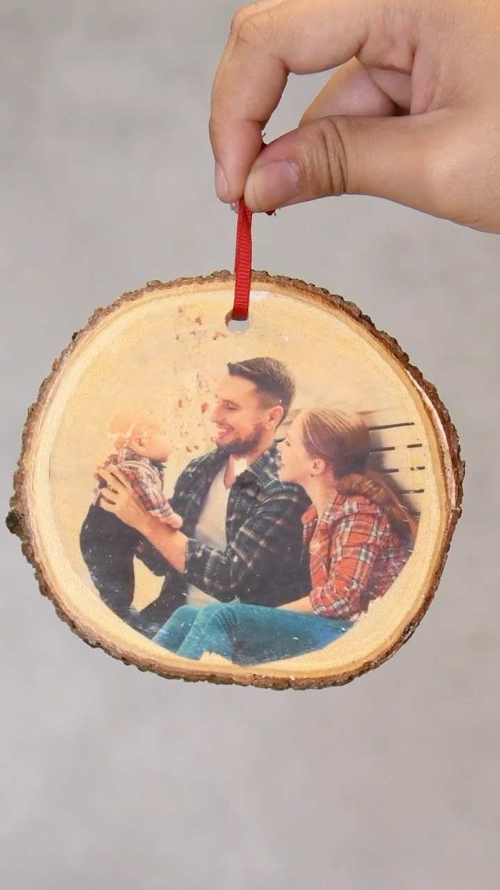 A hand holding a round wood slice ornament with a family photograph printed on it.