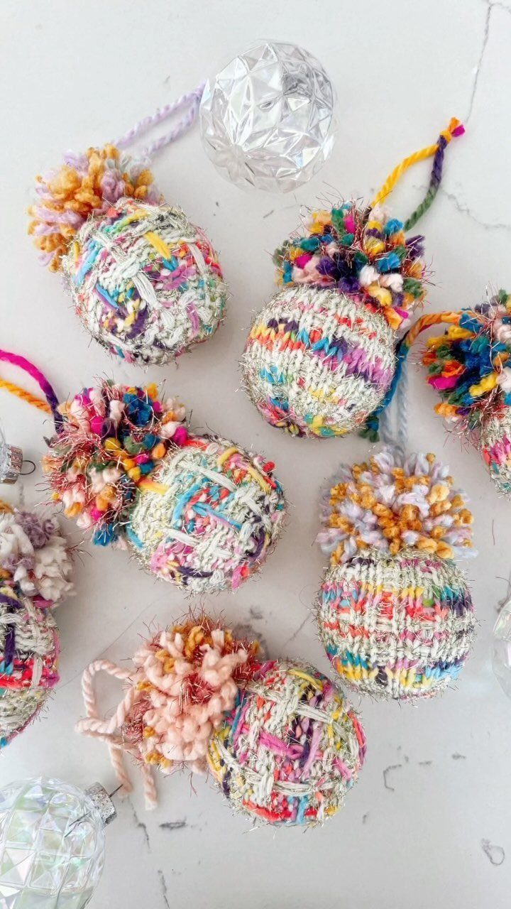 Colorful yarn-covered spherical ornaments with large multi-colored pom-poms scattered on a white background.