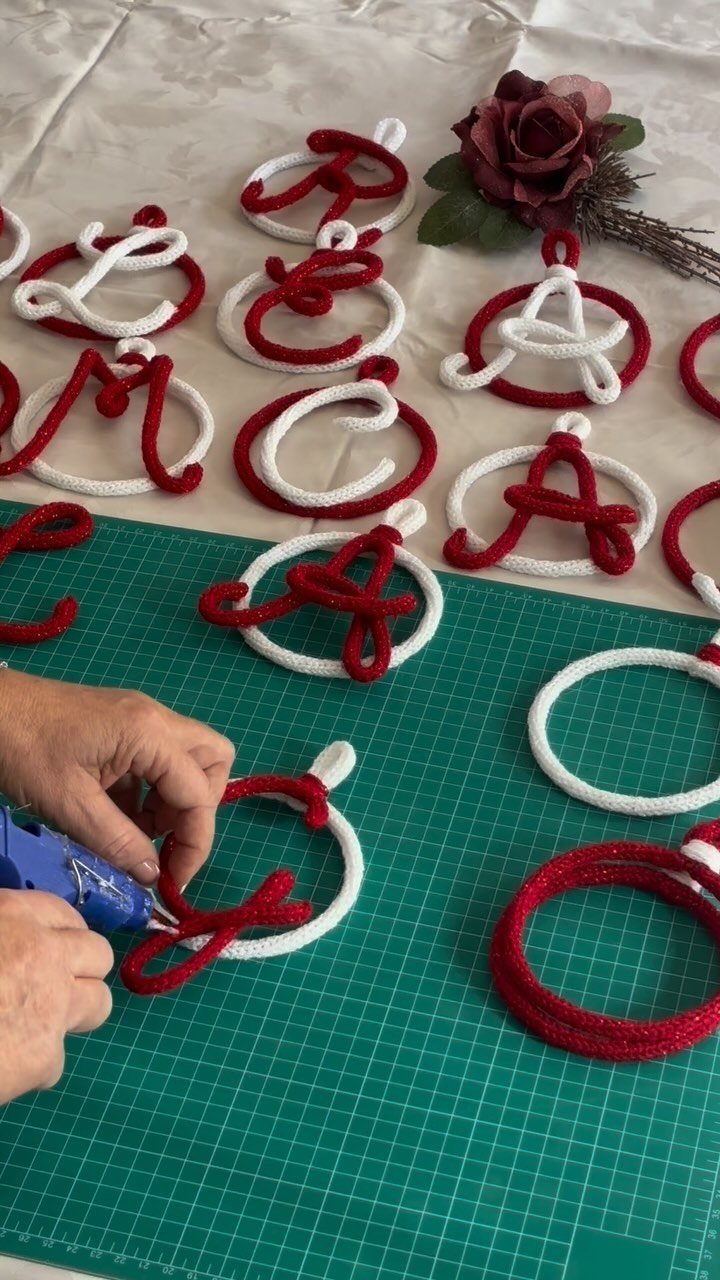 Hands using a glue gun to assemble red and white yarn-wrapped letter ornaments on a green mat.