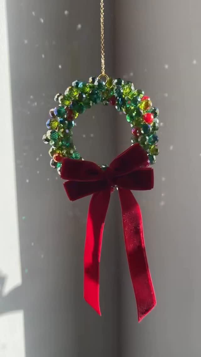A colorful beaded wreath ornament with a large red velvet bow hanging by a gold string.