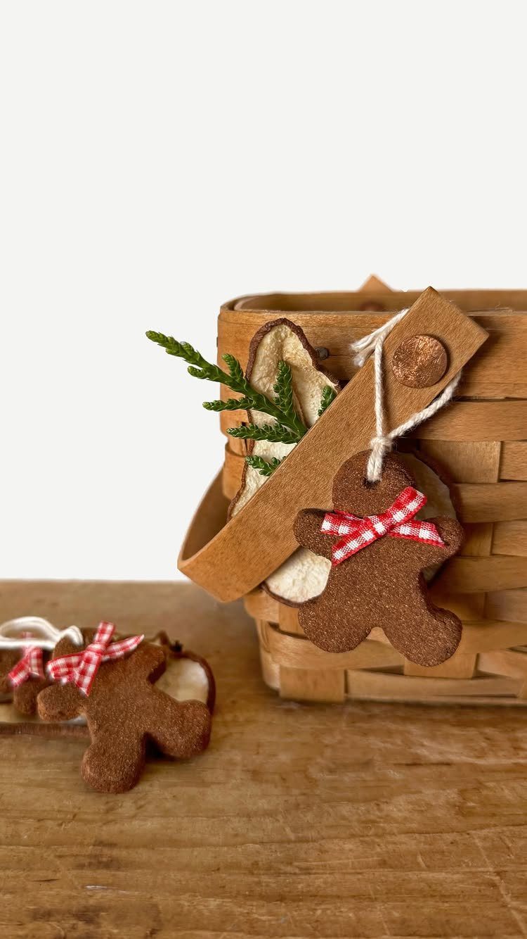 Gingerbread man shaped ornaments hanging from a wooden basket with red checkered bows.