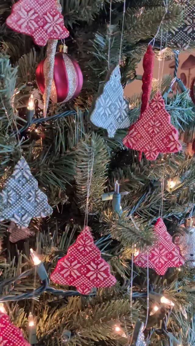 Fabric tree-shaped ornaments with sweater patterns hanging on a lit Christmas tree.