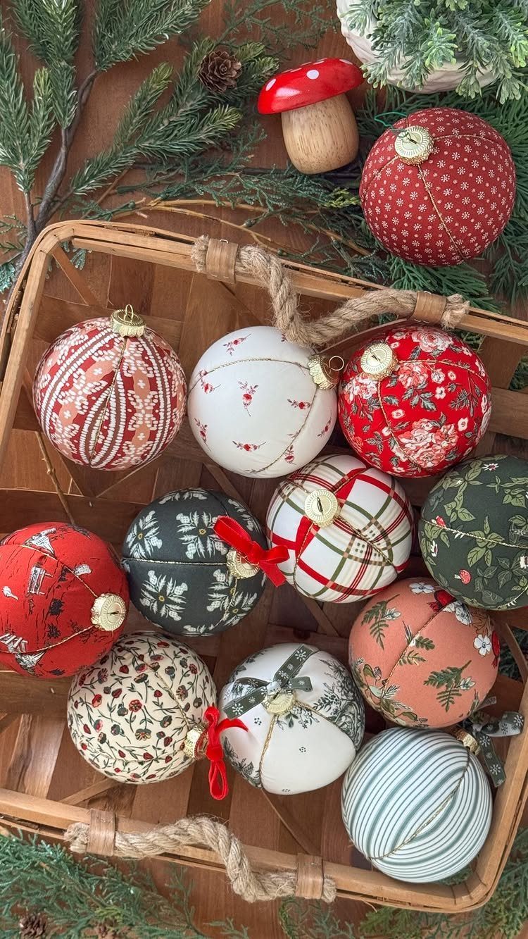 Fabric-covered Christmas ornaments with various patterns resting inside a wicker basket surrounded by pine branches.