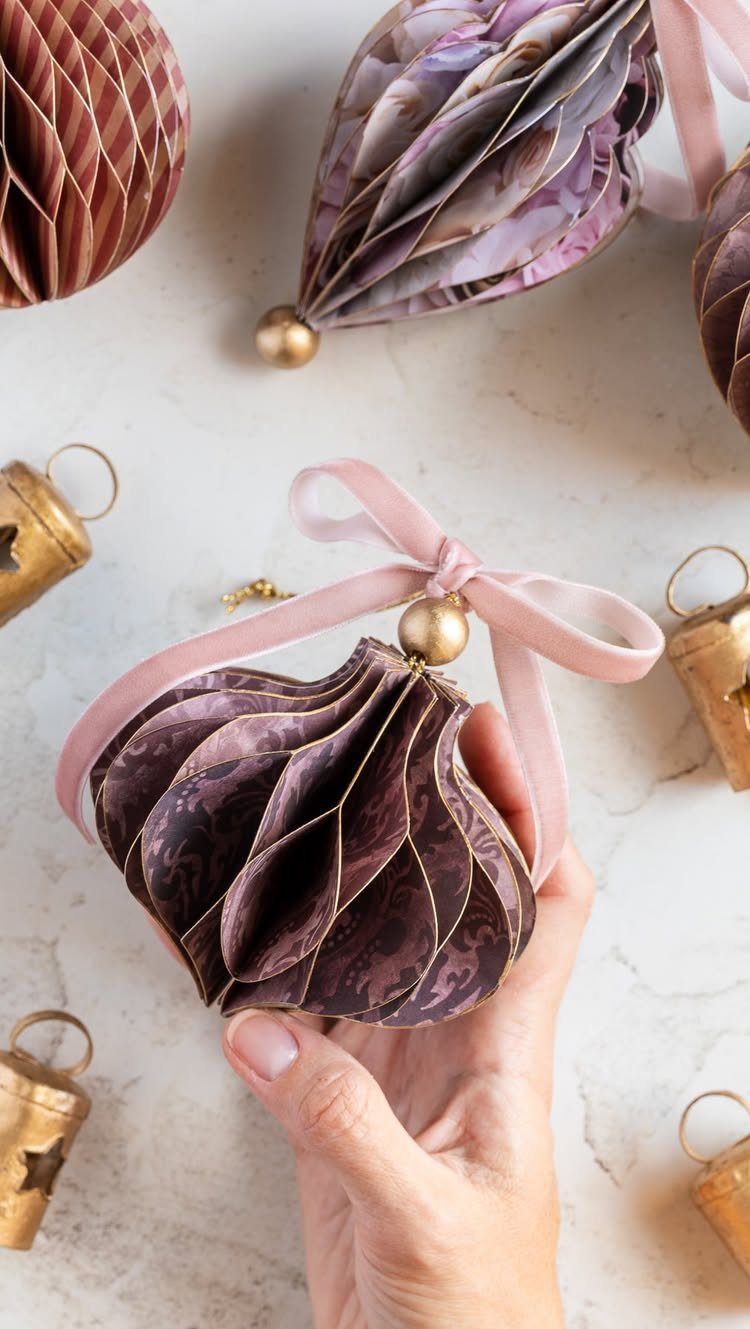 A hand holding a purple patterned paper honeycomb ornament with a pink ribbon.