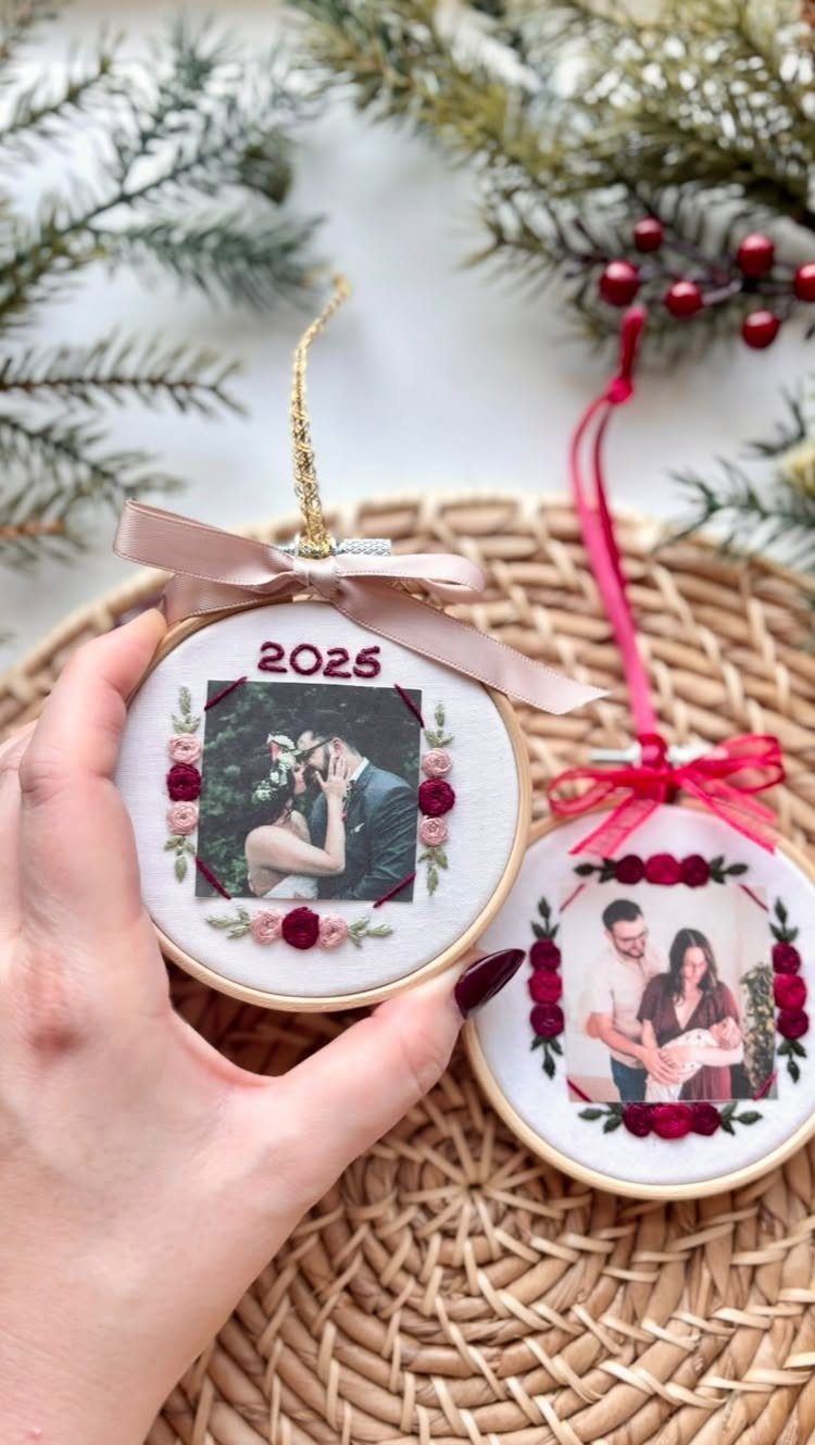 Hand holding a circular wooden ornament featuring a wedding photograph decorated with small red fabric flowers.