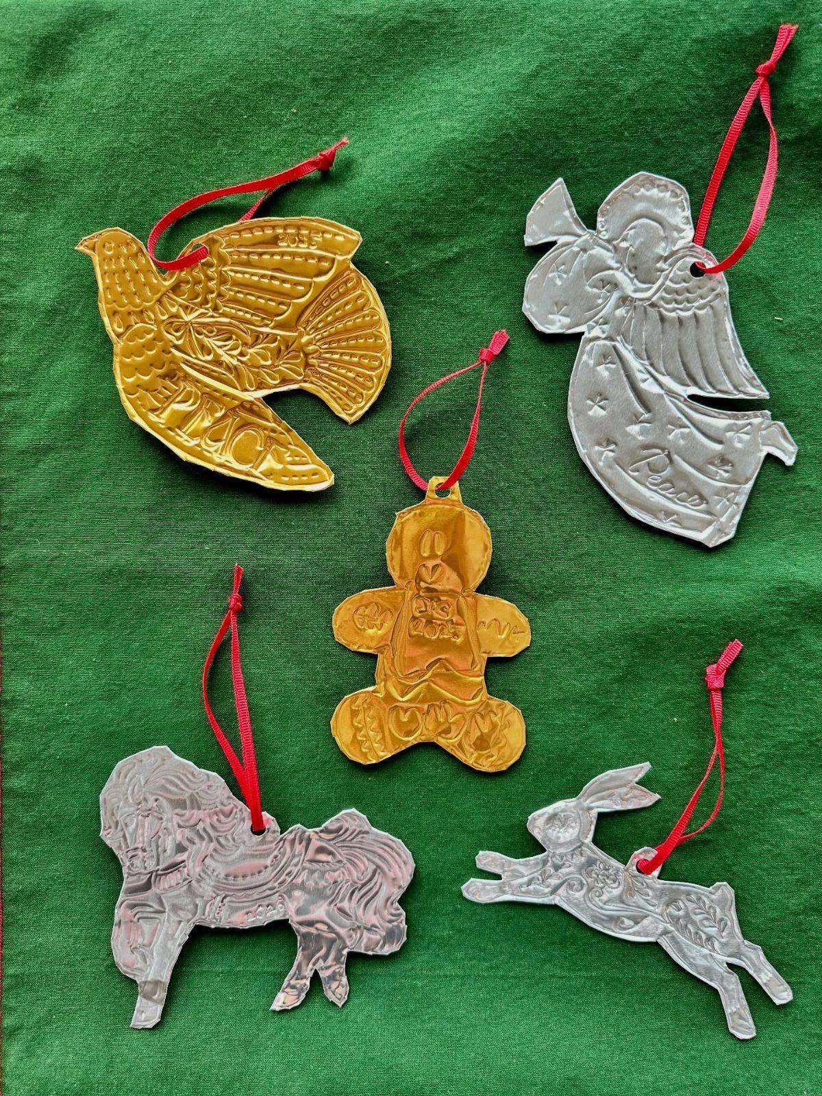 Five shiny gold and silver foil ornaments shaped like animals and figures on green fabric.