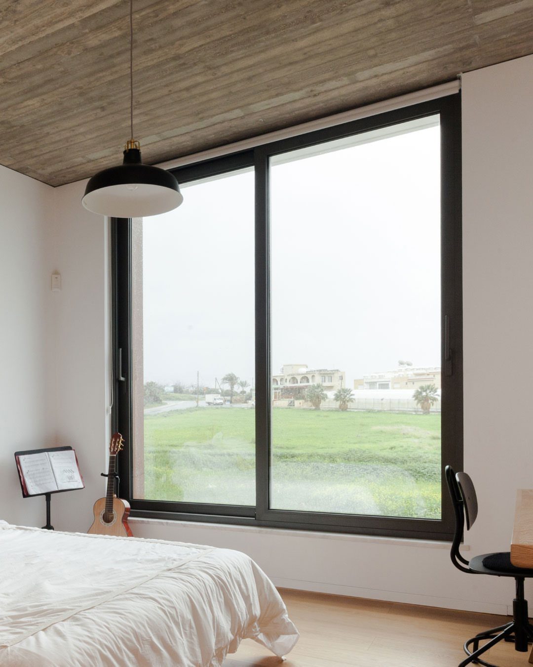 Front Window Design Ideas: 11 Looks Worth Stealing for 2026 1 A large black-framed sliding window overlooking a green field from a minimalist bedroom.