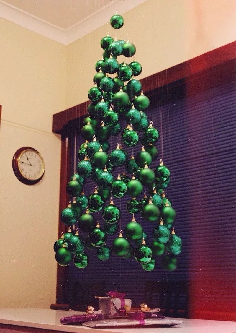 Hanging Christmas Tree: 6 Ideas for Small Spaces 1 Green Christmas ornaments hanging from the ceiling in a conical tree shape against a window.