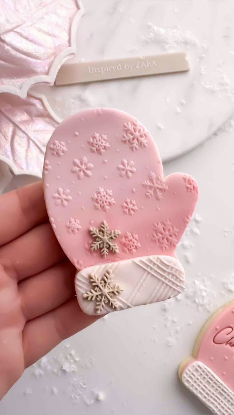 Homemade Christmas Decorations: 17 Easy Projects for 2026 2 A hand holding a pink mitten-shaped cookie decorated with white snowflake icing patterns.