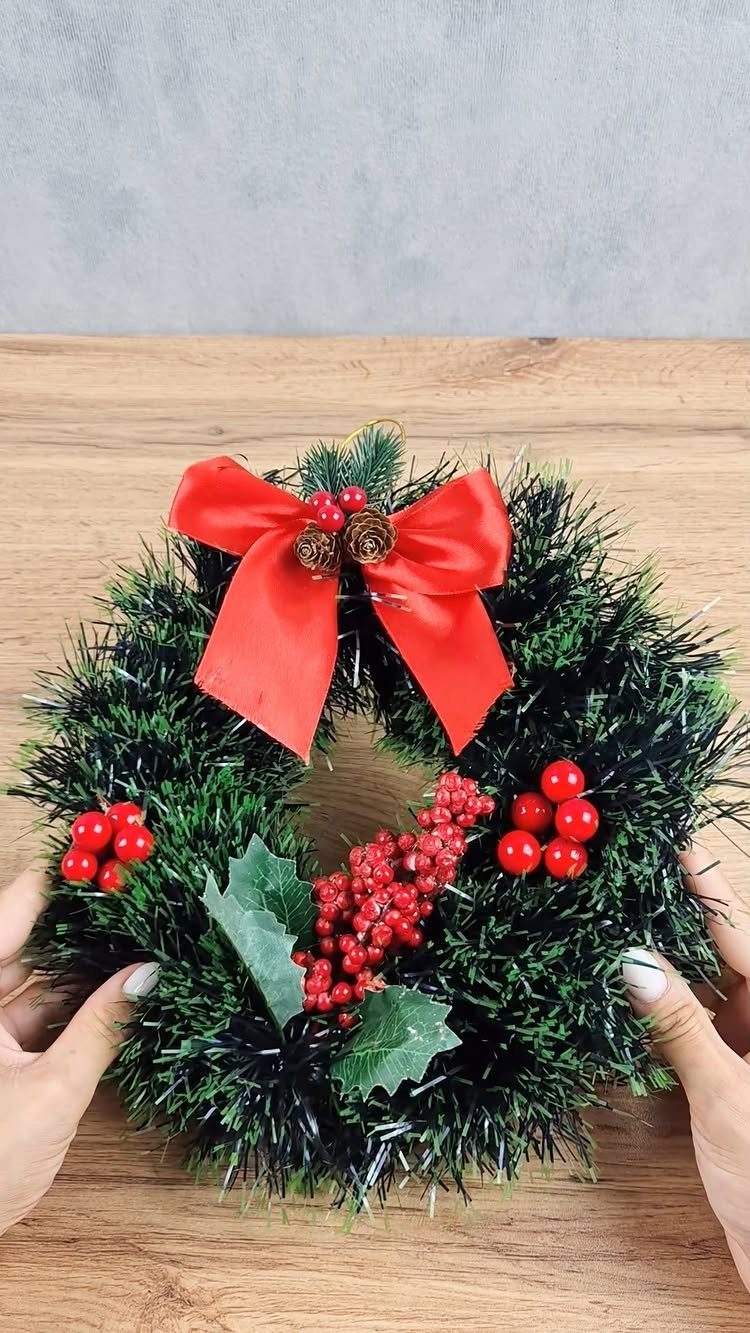 Homemade Christmas Decorations: 17 Easy Projects for 2026 6 A green tinsel wreath with a red bow and red berries held by two hands.