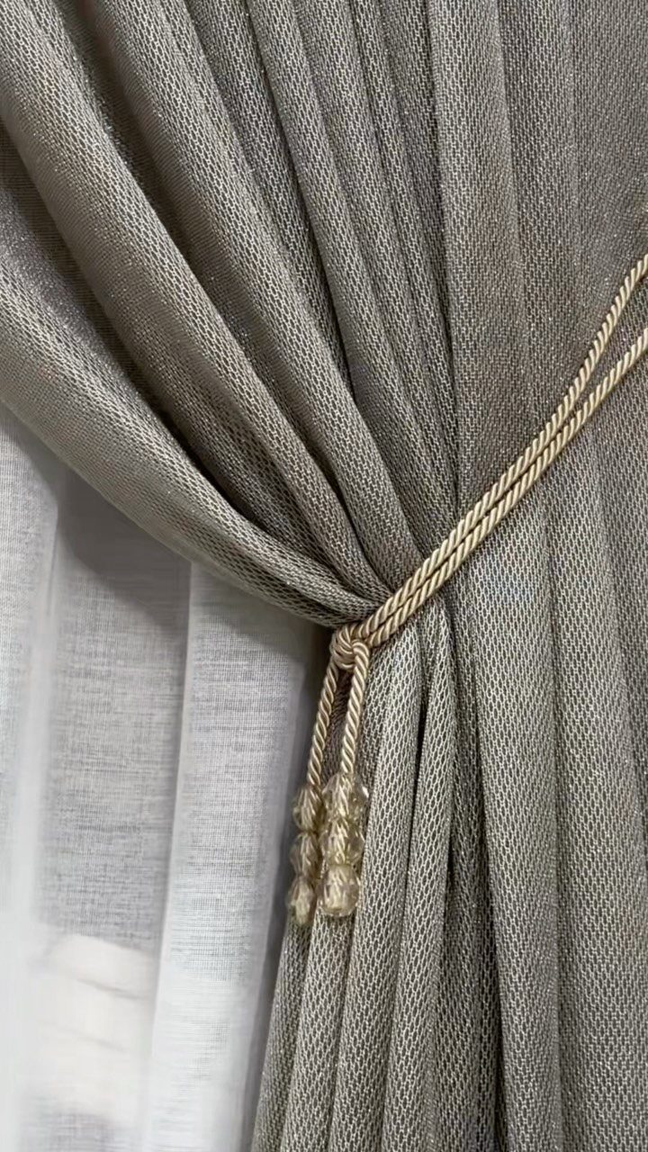 13 House Curtains Ideas for Every Style 11 Beige textured curtains gathered with a beaded rope tieback against a sheer white curtain.