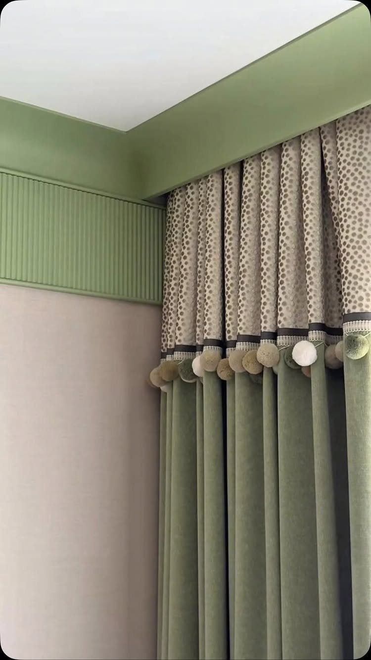 13 House Curtains Ideas for Every Style 10 Green velvet curtains with a patterned top section and decorative pom-pom trim hanging in a room.