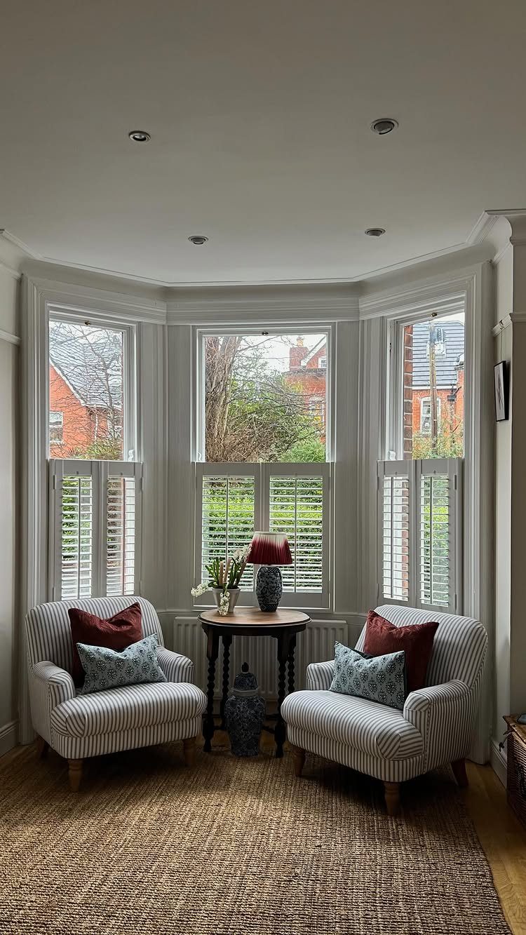 White cafe shutters installed on the lower portion of large bay windows in a living room.