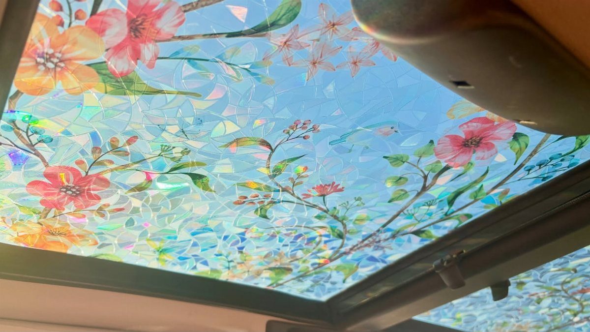 Floral mosaic pattern applied to a glass sunroof showing pink and yellow flowers against a blue sky.