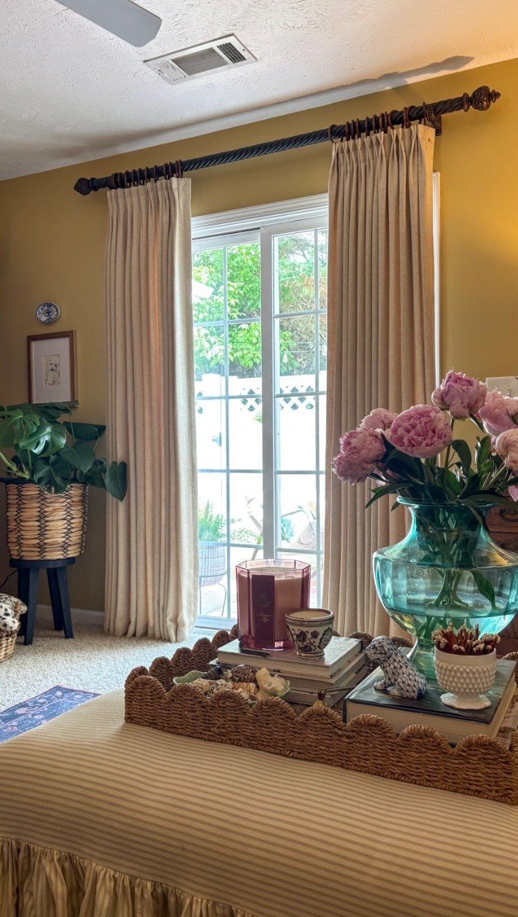Cream colored drapes hanging from a dark rod framing a sliding glass patio door.