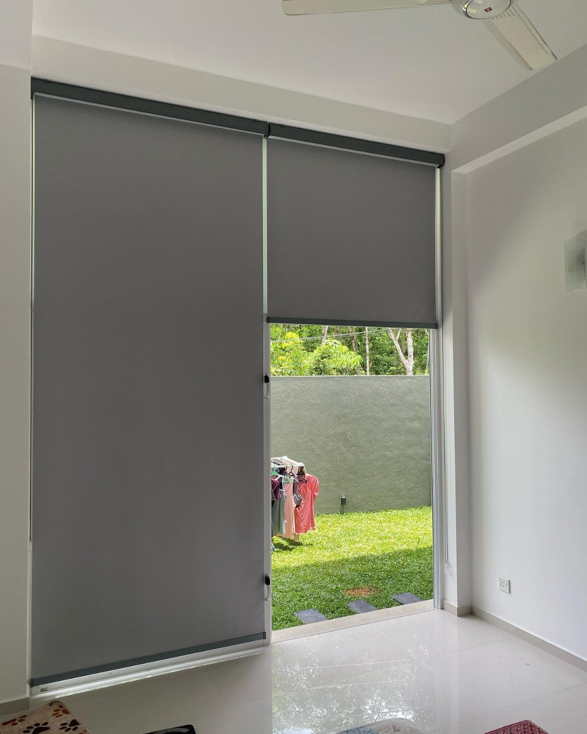 Two grey roller shades installed on a large glass patio door overlooking a green lawn.