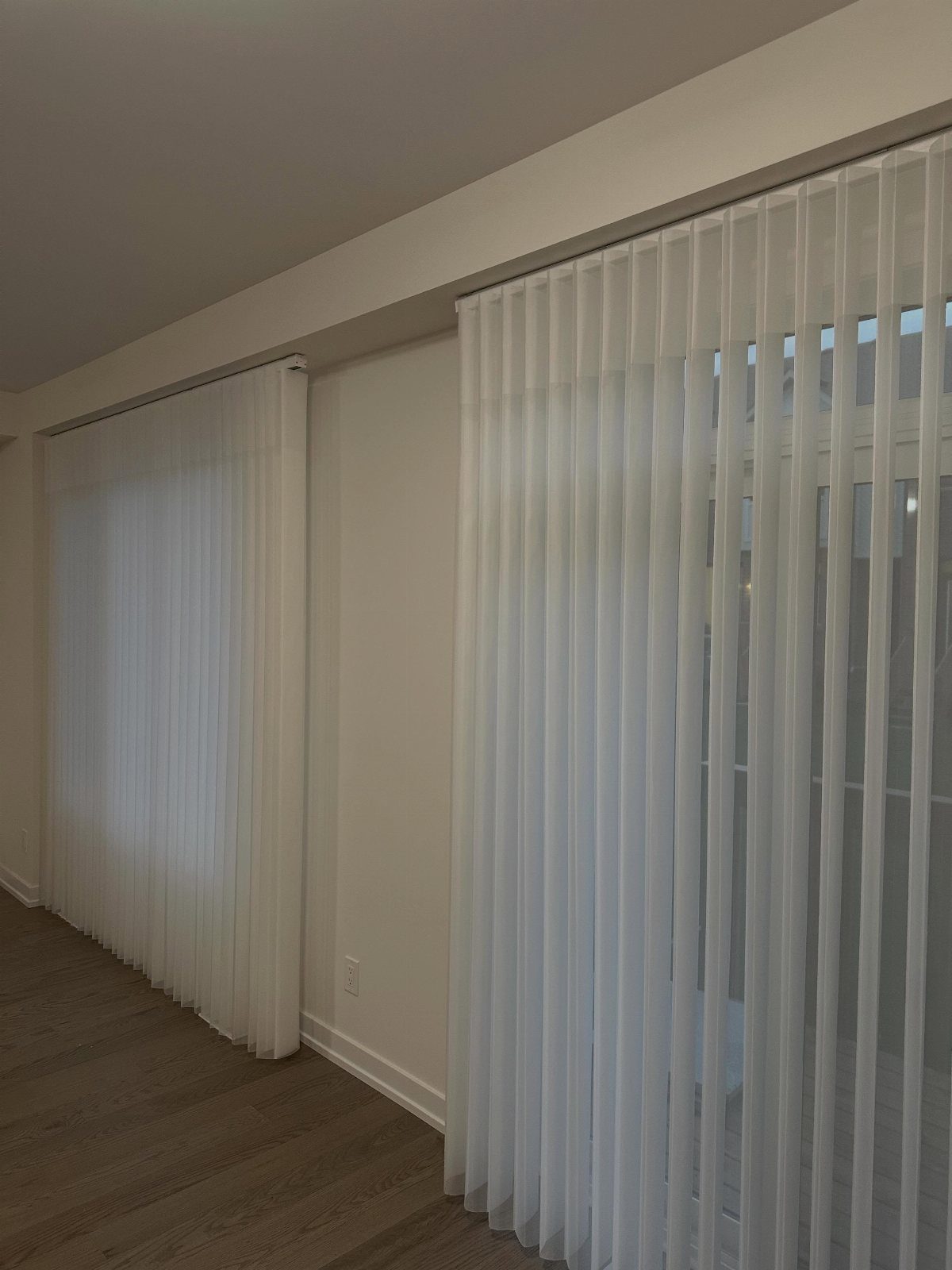 White sheer vertical shades covering large glass patio doors in a modern room.